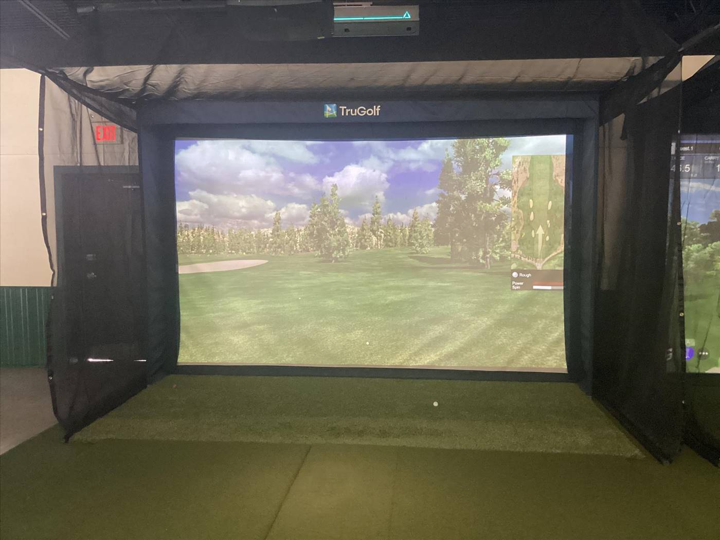TruGolf simulator bay with virtual golf course on large projection screen